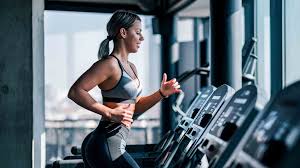 Woman jogging on a treadmill in a modern gym with large windows.